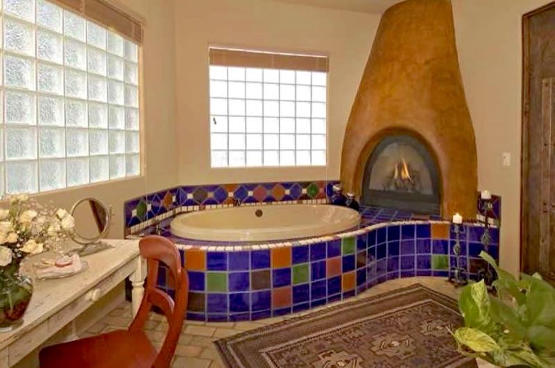 Hacienda villa two-person jetted tub in colorful tile beside a kiva fireplace